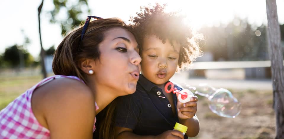 A child blows bubbles on a playground with his mother.