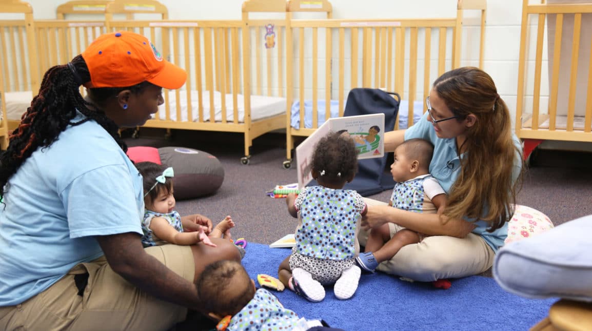 LENA Grow teachers sit on the floor of a classroom reading with infants.