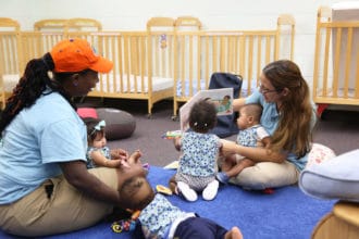 LENA Grow teachers sit on the floor of a classroom reading with infants.