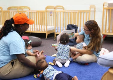 LENA Grow teachers sit on the floor of a classroom reading with infants.
