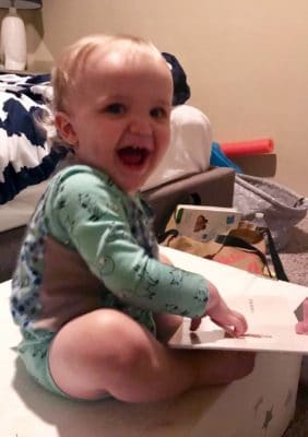 A baby smiles while reading a book.