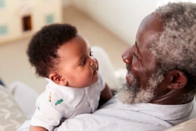 Proud Grandfather Cuddling Baby Grandson In Nursery At Home