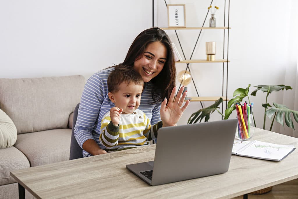 A mother and her child wave at a computer screen.