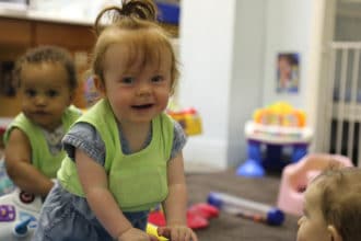 children smiling in toddler classroom wearing LENA vests