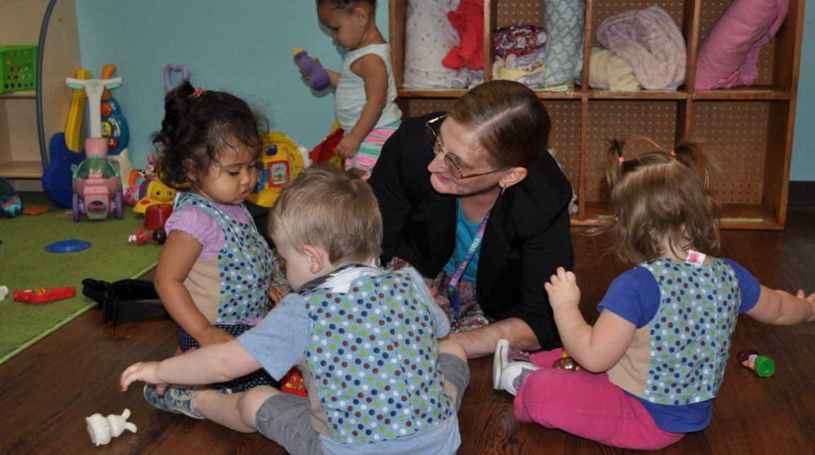 Early childhood educator sitting on the floor talking with a group of toddlers