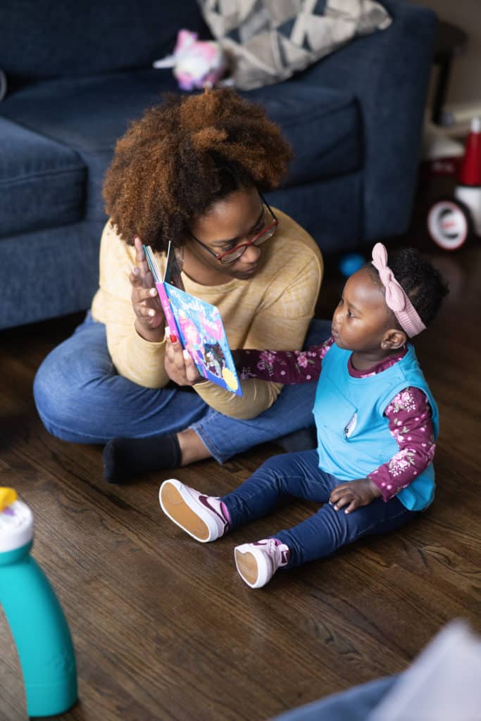 mother and daughter reading book on the floor