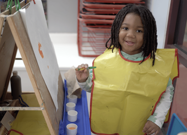 Preschooler in art smock smiling at the camera