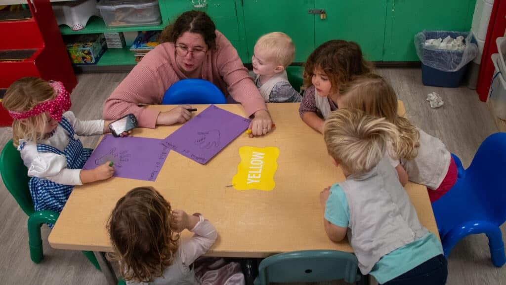 Teacher sitting with students while they talk and draw.