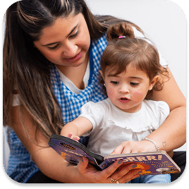 Woman and a young child sitting together and reading a children's book. The woman wears a blue checkered shirt, and the child has a white shirt with a small ponytail. The book has colorful illustrations and text.
