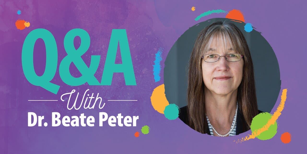 Q&A with Dr. Beate Peter written on a colorful purple background, next to a portrait of Dr. Beate Peter, a woman with long brown hair, glasses, and a necklace, wearing a dark jacket.