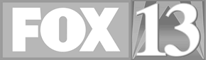The image shows the "FOX 13" logo in bold white letters on a gray background. The letters "FOX" are in a box to the left, with the number "13" prominently displayed to the right.