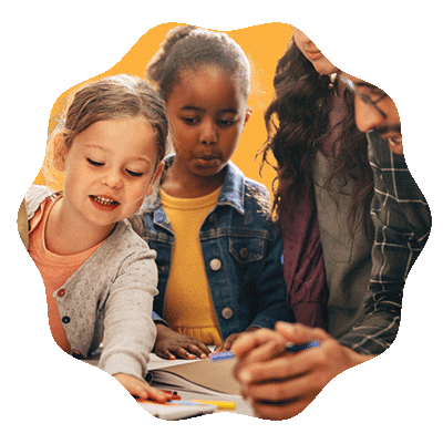 Three young children and an adult sit together at a table, looking engaged as they work on a creative activity with papers and colored markers. The background is a solid orange color.