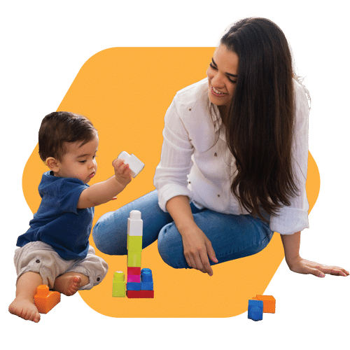 A woman sitting on the floor smiling at a baby who is playing with colorful building blocks, with a yellow geometric shape in the background.