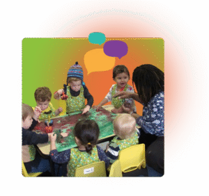 A group of young children wearing aprons sit around a table doing a craft with an adult. The background is a colorful gradient with overlapping speech bubbles.